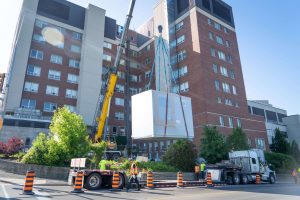 Crane lifting air handling unit on a bright day in front of the Brantford General Hospital.